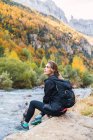 Вид сбоку на женщину-туристку с рюкзаком, сидящую на валуне у реки в горах Пьяхес во время отдыха в национальном парке Ордеса и Пердидо — стоковое фото
