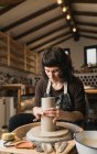 Орієнтована жінка-художниця створює глиняний посуд на керамічному колесі під час роботи в художній студії — стокове фото