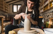 Artesana femenina enfocada creando vajilla de barro sobre rueda de cerámica mientras trabaja en estudio de arte - foto de stock