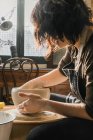 Побочный обзор сфокусированной неузнаваемой женщины-ремесленницы с помощью гончарного колеса и создание ручной глиняной посуды в мастерской — стоковое фото