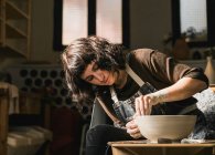 Fokussierte Kunsthandwerkerin mit Töpferscheibe und handgefertigtem Steingut in Werkstatt — Stockfoto