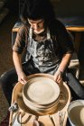 Зверху зосереджена жінка-художниця, що використовує гончарне колесо та створює глиняний посуд ручної роботи в майстерні — стокове фото