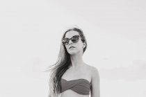 Уверенная в себе длинноногая хипстерша-подросток в стильном летнем наряде и солнечных очках, наслаждающаяся летними каникулами на море — стоковое фото