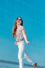 Low angle of cheerful carefree young female in sunglasses wearing casual striped t shirt and jeans enjoying sunny summer day — Stock Photo