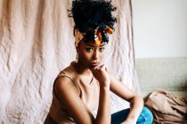 Vista laterale calma femmina nera in fascia alla moda e con acconciatura Afro appoggiata sulle mani e guardando la fotocamera su sfondo beige — Foto stock