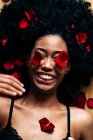 Draufsicht auf eine romantische, fröhliche Afroamerikanerin, die mit roten Rosenblättern auf dem Boden liegt, mit geschlossenen Augen — Stockfoto