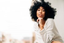 Side view of peaceful African American female with curly hair leaning on railing while standing on balcony and looking at camera — Stock Photo