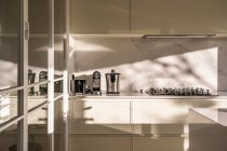 Интерьер современной домашней кухни с легкой мебелью и зеркальными элементами при дневном свете — стоковое фото