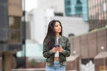 Стильная азиатка в модной камуфляжной куртке просматривает мобильный телефон на городской улице — стоковое фото