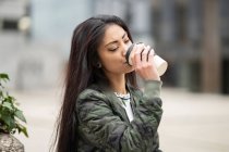 Young Asian female in stylish outfit enjoying coffee to go in weekend in park — Stock Photo
