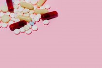 Куча разноцветных капсул и таблеток разных размеров, размещенных на розовом фоне — стоковое фото