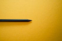 Composición minimalista vista superior con lápiz negro dispuesto sobre fondo amarillo con espacio vacío - foto de stock