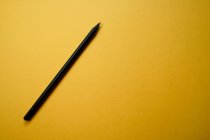 Composición minimalista vista superior con lápiz negro dispuesto sobre fondo amarillo con espacio vacío - foto de stock
