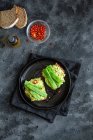 Аппетитные тосты со свежим гуакамоле и зеленым горохом, украшенные красным перцем и подаваемые на черной тарелке — стоковое фото
