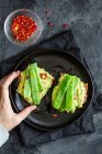 Top view raccolto anonimo femminile azienda gustosi toast freschi con guacamole e piselli verdi serviti su piatto nero — Foto stock