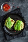 Torradas apetitosas com guacamole fresco e vagens de ervilhas verdes decoradas com pimentas vermelhas e servidas em prato preto — Fotografia de Stock