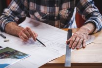 Анонімний чоловічий архітектор сидить за столом на кухні і малює план будівлі з олівцем і лінійкою під час роботи вдома — стокове фото