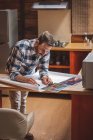 Encantado arquitecto masculino de pie a la mesa y plano de dibujo de la casa en papel mientras trabaja en el proyecto en casa - foto de stock