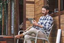 Side view of busy male architect sitting on chair on terrace with blueprint and browsing tablet while working on project — Stock Photo