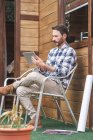 Вид збоку зайнятого чоловіка архітектора, який сидить на стільці на терасі з відбитками і планшетом під час роботи над проектом — стокове фото