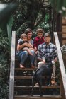 Cheerful couple with children sitting on wooden steps of modern house together with dog — Stock Photo