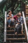 Alegre pareja con niños sentados en escaleras de madera de la casa moderna junto con el perro - foto de stock