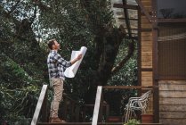 Low angle side view of male architect with paper draft standing on terrace of wooden house in forest — Stock Photo