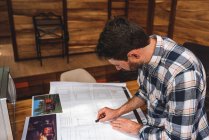 From above side view of male architect drawing blueprint of building while working on project at home — Stock Photo