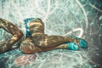 Crop young female in casual clothes lying in abstract light projection of tangled white lines — Stock Photo