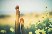 Mujer anónima en zapatos de verano balanceo piernas contra la proyección de campo con flores amarillas - foto de stock