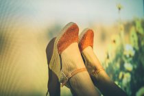 Анонимная женщина в летних туфлях, размахивающая ногами против проекции поля с желтыми цветами — стоковое фото