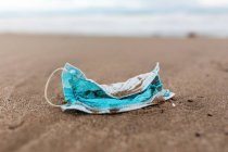 Used protective mask on beach washed by sea wave showing concept of environmental pollution with medical waste — Stock Photo
