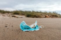 Gebrauchte Schutzmaske am Strand, angespült von Meereswellen, die das Konzept der Umweltverschmutzung mit medizinischen Abfällen aufzeigt — Stockfoto
