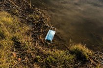 De cima da máscara médica plástica que flutua na água da lagoa que mostra o conceito da poluição ambiental com plástico — Fotografia de Stock