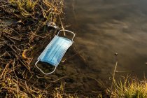 Зверху пластикова медична маска, що плаває на воді ставка, що показує концепцію забруднення навколишнього середовища пластиком — стокове фото