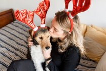 Happy female in decorative deer horns cuddling adorable purebred dog on bed — Stock Photo