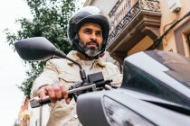De baixo de brutal etnia masculina motociclista no capacete de condução contemporânea moto enquanto olha para a frente na cidade — Fotografia de Stock