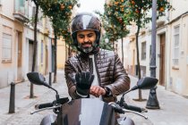 Mature barbu hispanique mâle motard dans un casque de protection portant un gant sur moto contemporaine sur la rue — Photo de stock