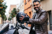 Vue latérale du contenu masculin Hispanique mâle motocycliste avec casque regardant loin sur la moto en ville — Photo de stock