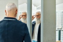 Вид сзади на стильного мужчину, стоящего перед зеркалом в оптическом магазине и примеряющего модные очки — стоковое фото