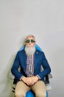 Maschio anziano barbuto in occhiali da test oculari seduto in clinica moderna prima dell'esame della vista e guardando la fotocamera — Foto stock