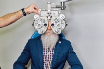 Crop óptico irreconhecível usando phoropter para teste de visão de paciente do sexo masculino sênior na clínica — Fotografia de Stock