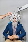 Cosecha óptico irreconocible utilizando phoropter para la prueba de la vista del paciente masculino de edad avanzada en la clínica - foto de stock