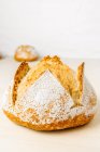 Вкусный хлеб круглой формы с мукой на золотой поверхности в пекарне на белом фоне — стоковое фото