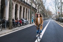 Fröhliche Frau im Mantel schaut mit Fahrrad gegen Altbau mit Säulen in der Stadt — Stockfoto
