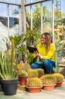 Giardiniere femminile utilizzando tablet moderno, mentre il conteggio delle piante e lavorare nel centro del giardino — Foto stock