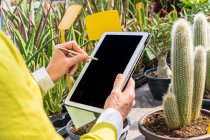 Coltiva giardiniere femminile utilizzando tablet moderno mentre conta le piante e lavora nel centro del giardino — Foto stock