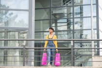 Encantada afro-americana fêmea de pé com sacos de papel na cidade e olhando para longe depois de compras bem sucedidas — Fotografia de Stock