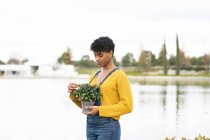 Gioiosa donna afroamericana in piedi con rami con fiori in parco in primavera e guardando la fotocamera — Foto stock