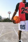Cortado jogador de streetball masculino afro-americano irreconhecível em uniforme de pé com bola na quadra de basquete — Fotografia de Stock